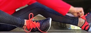 Woman sitting down in exercise gear tying her shoe.