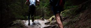 Two men running on a uphill trail in the woods for exercise.