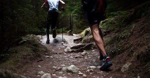 Two men running on a uphill trail in the woods for exercise.