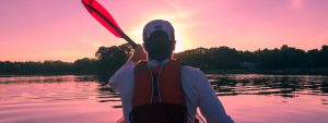 Man kayaking in a serene lake at sunset.