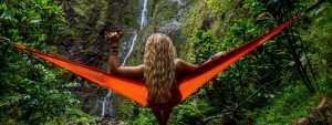 Woman in a tropical setting relaxing in a hammock looking at waterfalls.